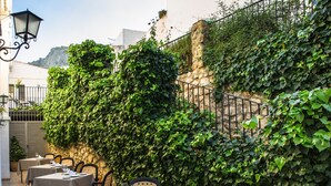 An outdoor dining area with tables and chairs, surrounded by lush greenery and stone walls. - Hotel Rural Zuhayra (Zuheros)