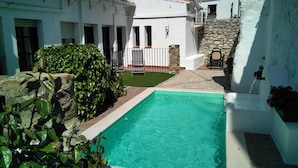 A pool area with a white building, stone walls, and a small lawn. - Hotel Rural Zuhayra (Zuheros)