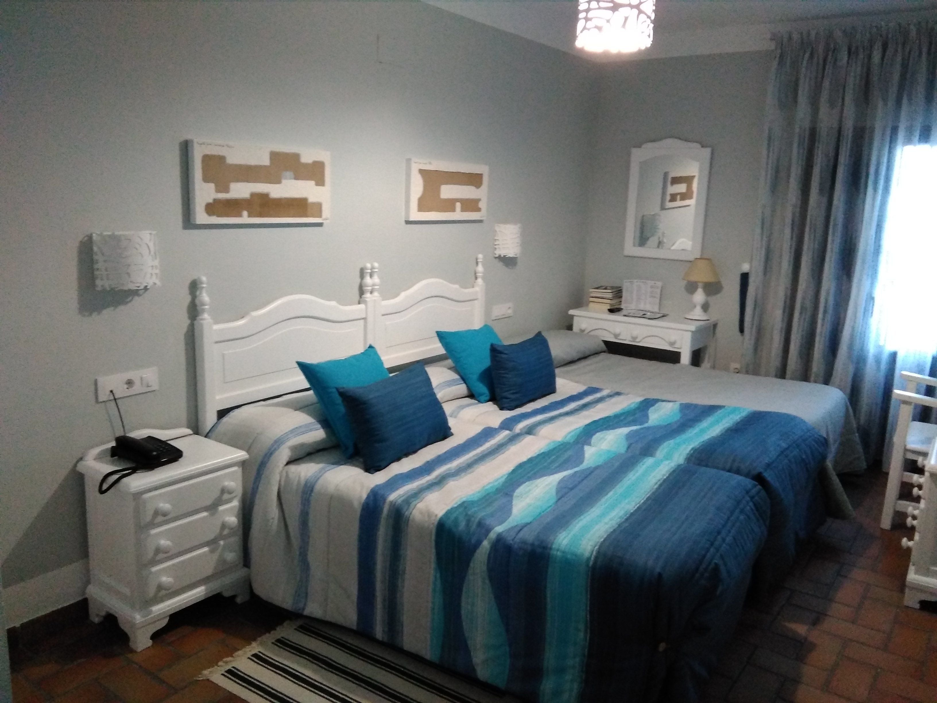 A bedroom with two beds, a nightstand, a dresser, and a window with curtains.