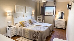 A hotel room with two beds, a nightstand, a dresser, and a window with a view. - Hotel Rural Zuhayra (Zuheros)