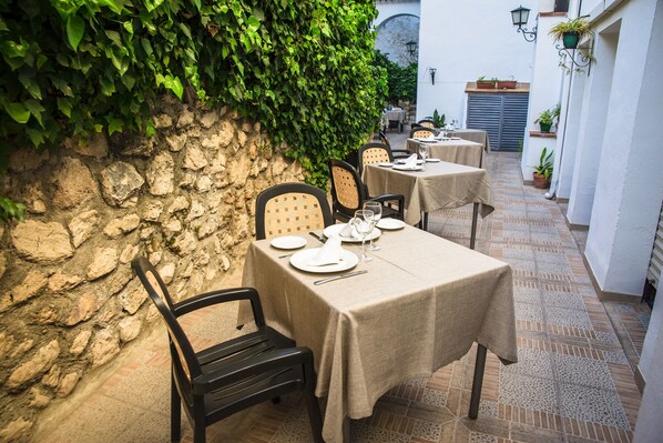 An outdoor dining area with stone walls, tables set with white tablecloths, and chairs. - Hotel Rural Zuhayra (Zuheros)