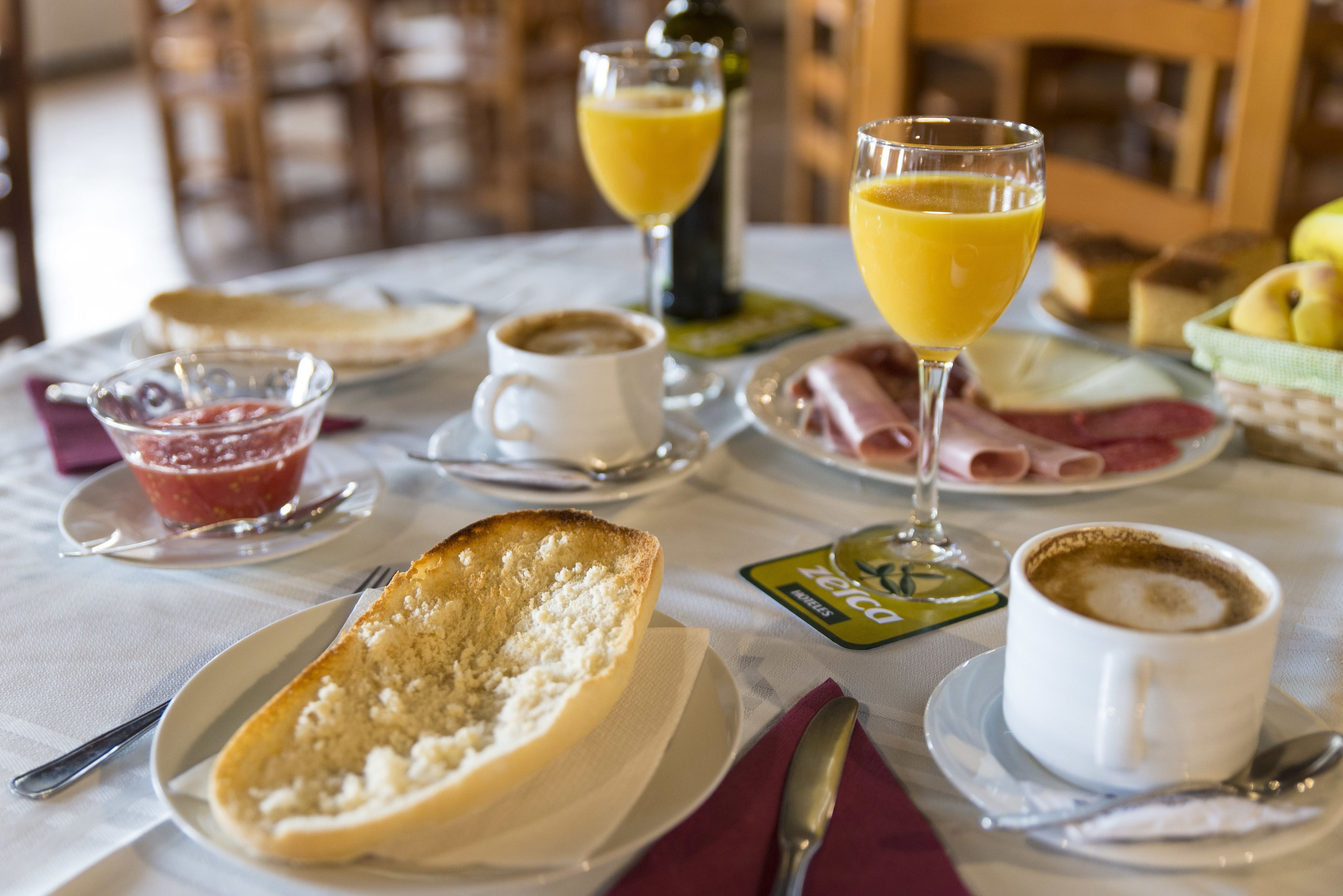 Une table de petit-déjeuner avec des tartines, de la confiture, du café, du jus d’orange et diverses pâtisseries.