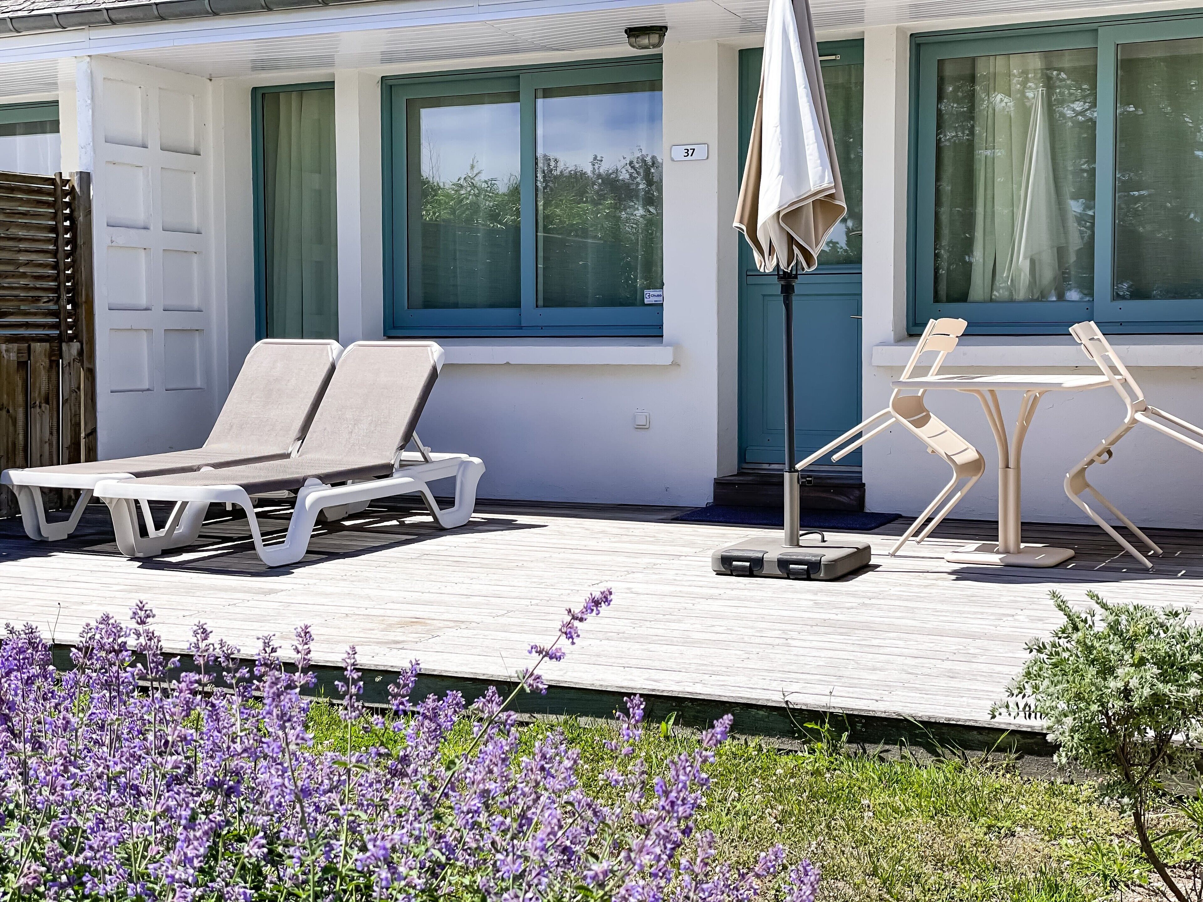 Ett soligt utomhusområde med två solstolar, ett bord med stolar och ett litet parasoll.