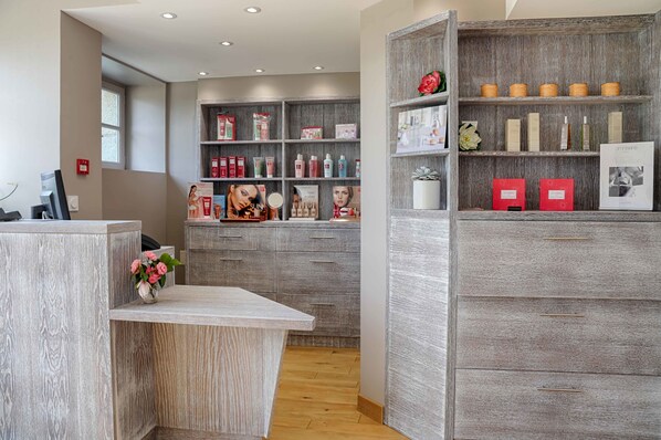 A reception area with a wooden reception desk, a counter, and shelves with various products. - Hotel Du Tumulus (Carnac)
