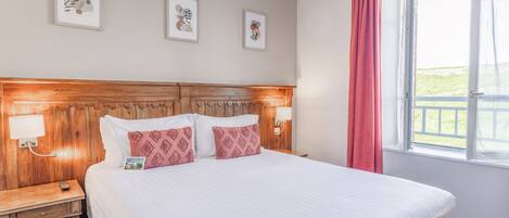 A neatly made bed with a wooden headboard, two bedside tables with lamps, and three framed artworks on the wall.