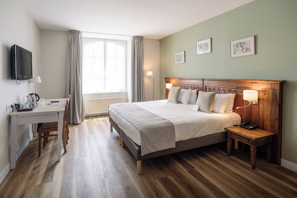 Habitación de hotel con cama, mesita de noche, lámpara, escritorio con silla y televisor.