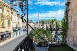 A balcony with a view of a street, a potted plant, and a metal railing.