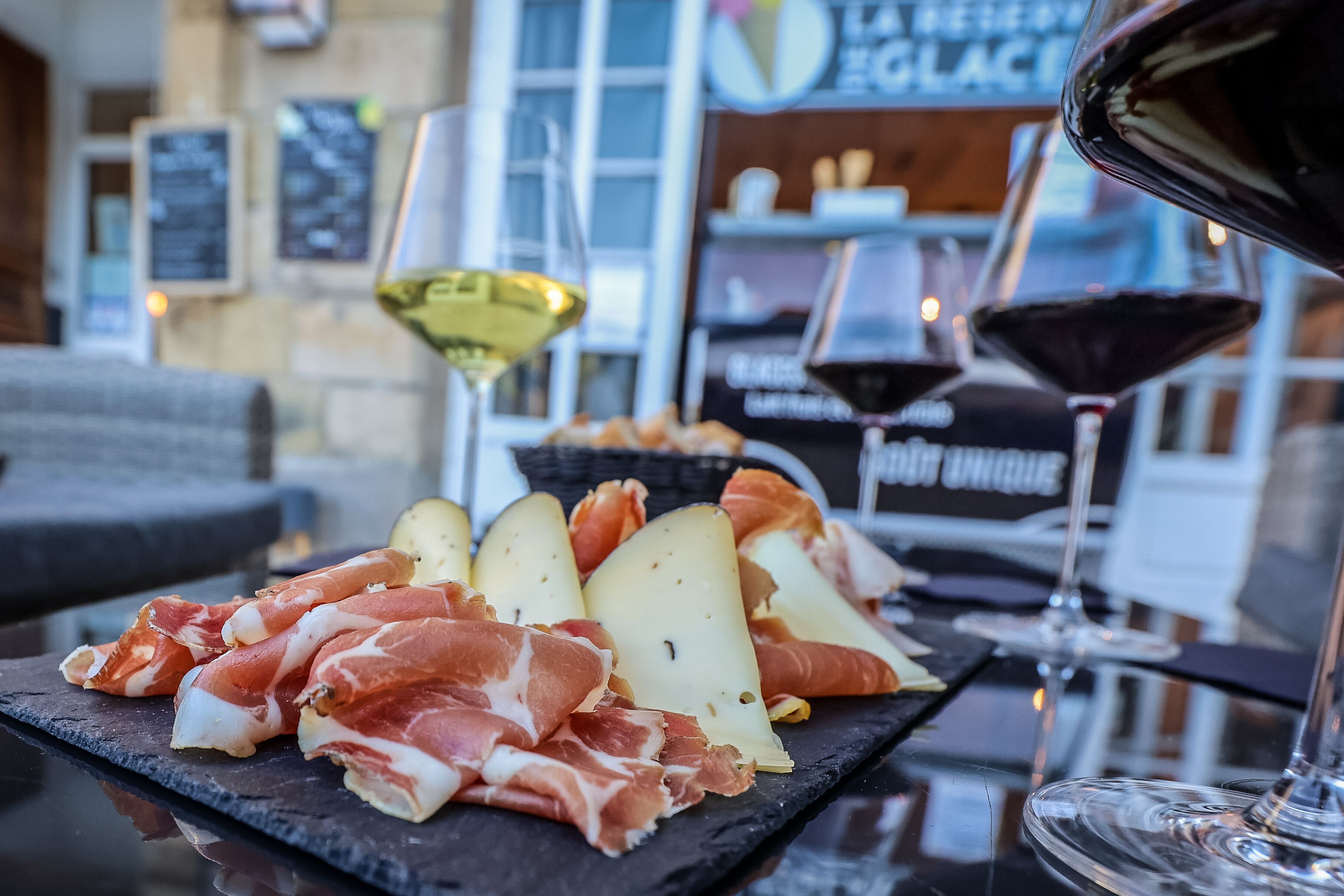 A selection of cured meats and cheeses on a slate board, accompanied by glasses of wine, set on a table in a restaurant.