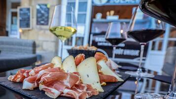 A selection of cured meats and cheeses on a slate board, accompanied by glasses of wine, set on a table in a restaurant.