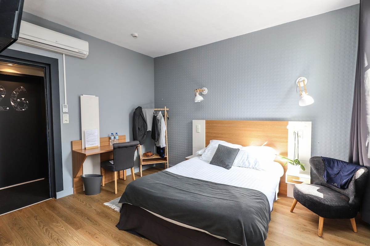 A hotel room with a bed, a desk, a chair, a wardrobe, and a bedside table.