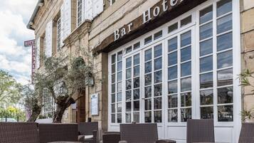 A Bar Hotel with wicker furniture outside, a sign indicating a Hotel Restaurant, and a large window reflecting the surroundings.