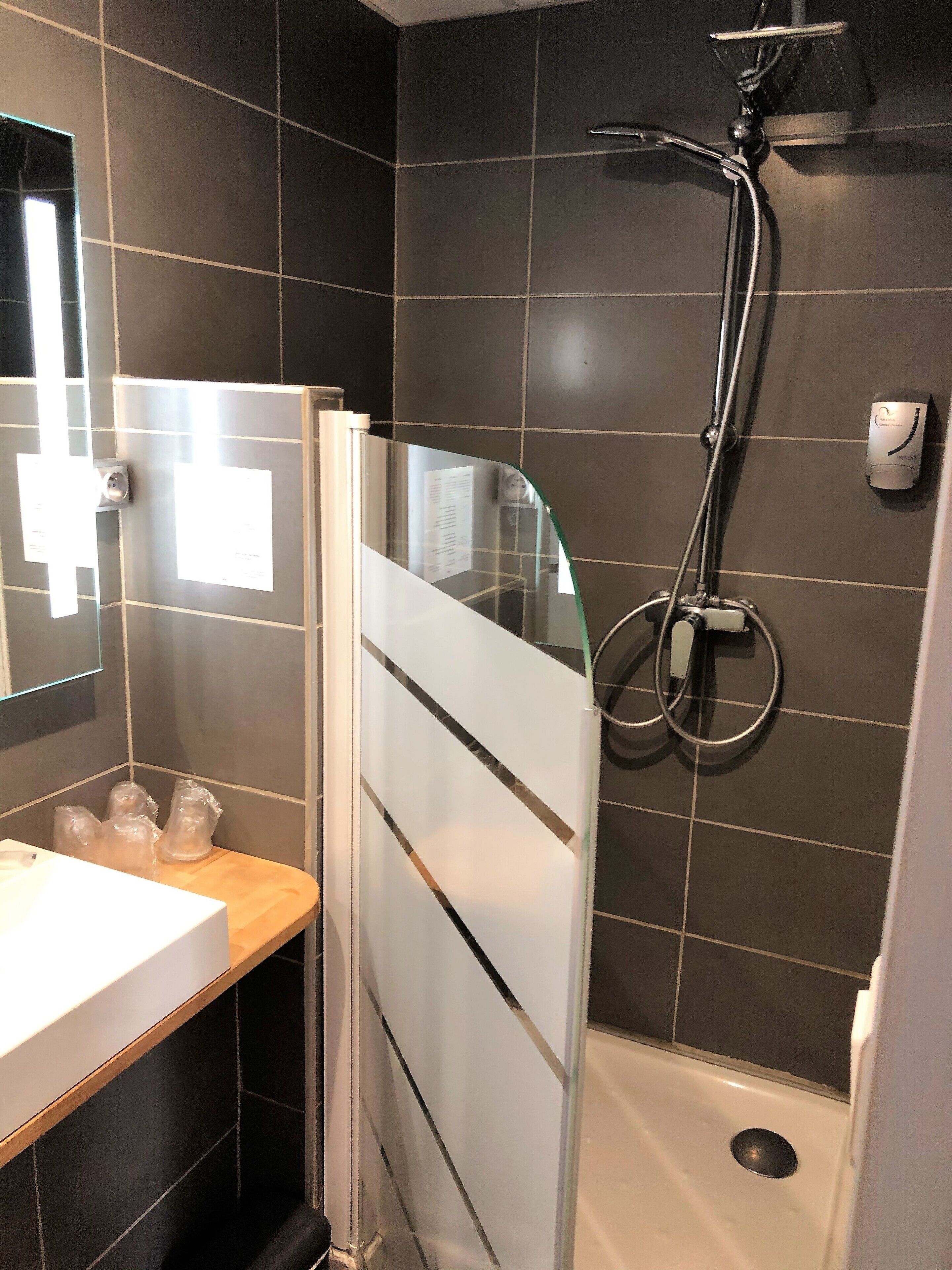 A modern bathroom with a glass shower enclosure, a white sink, and a mirror.