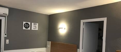 Un dormitorio con cama, una lámpara fijada a la pared y una puerta que da a un baño.