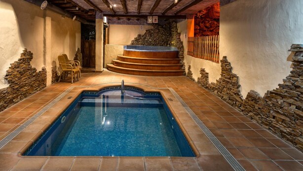 Piscina com muro de pedra e deck de madeira.