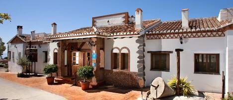 A traditional building with a tiled roof, a stone facade, and a small garden area with potted plants.