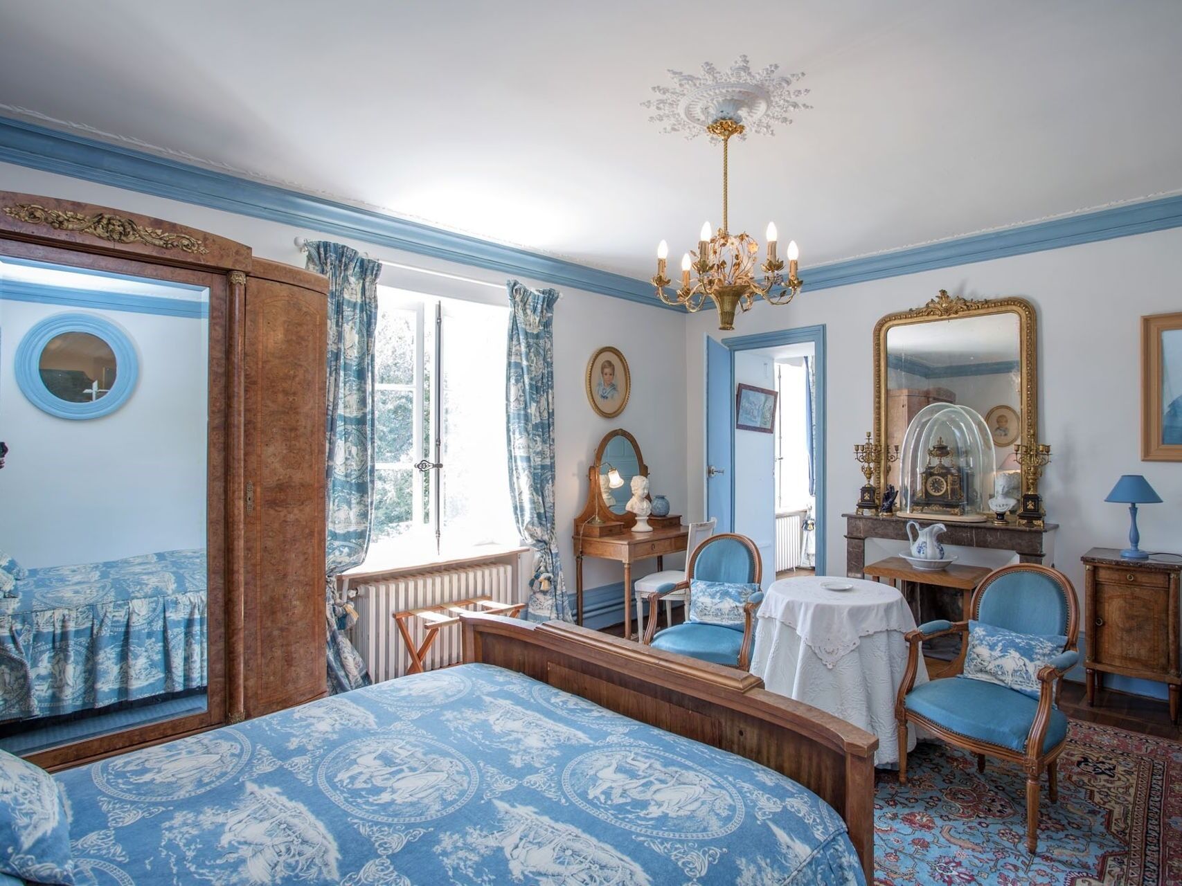 A bedroom with a large bed, a dresser, a chair, a mirror, and a chandelier.