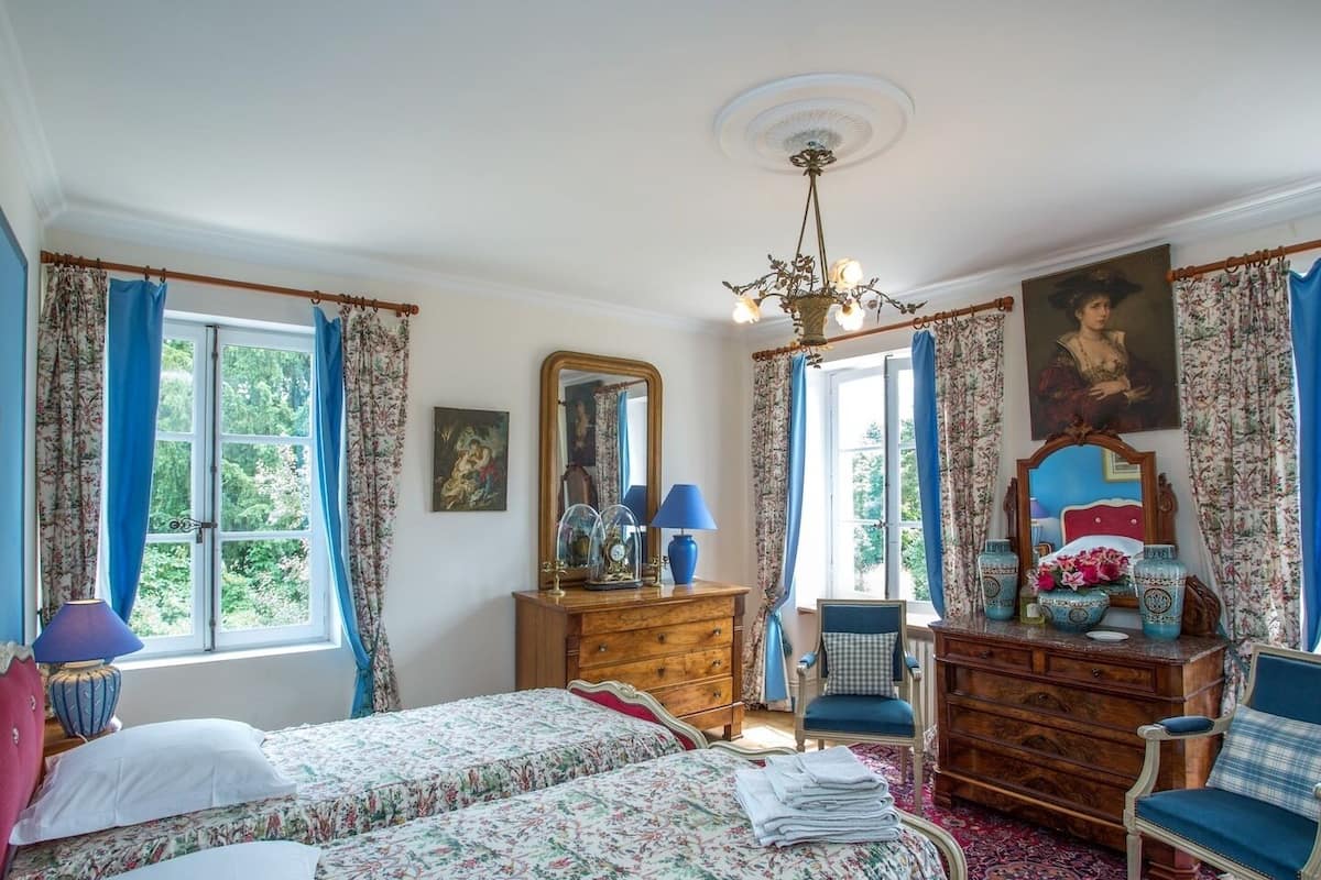Une chambre avec deux lits, une commode, une chaise, un miroir et un lustre.