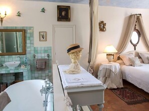 Experience a classic hotel room with a large bathtub, comfortable bed, and elegant furnishings.