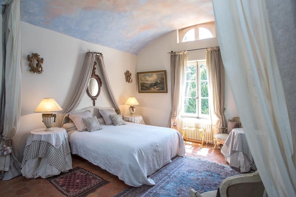 Une chambre à coucher avec un grand lit, deux tables de chevet, une fenêtre avec des rideaux, une fresque au plafond et un tableau au mur.