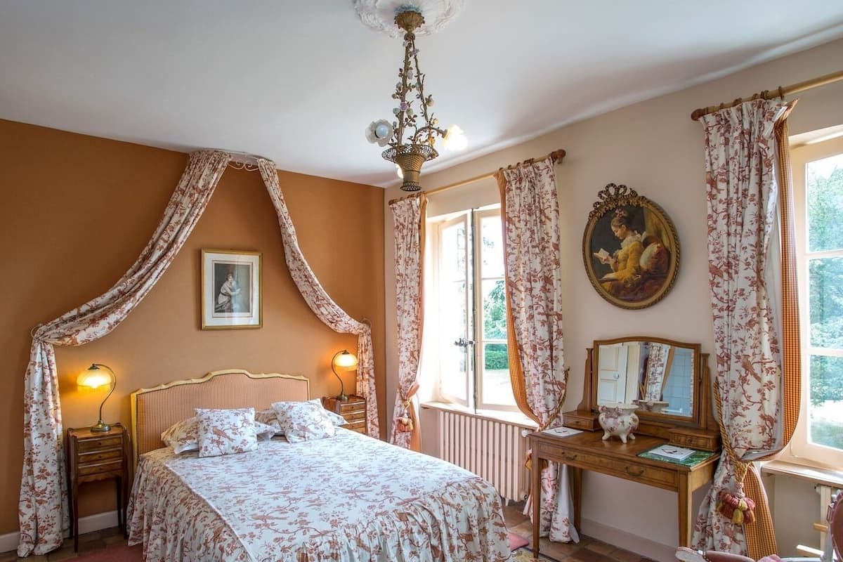 Une chambre à coucher avec un lit à baldaquin, un bureau avec un miroir et une fenêtre avec des rideaux.