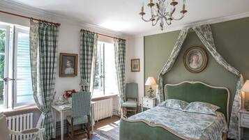 A bedroom with a green canopy bed, a chandelier, checkered curtains, and a view of the outdoors.