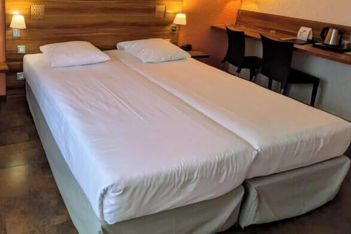 Habitación de hotel con dos camas, cabecera de madera, escritorio con sillas y una lámpara.