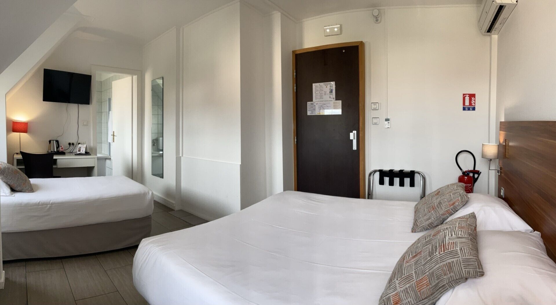 A hotel room with two beds, a desk, a TV, and a bathroom visible through an open door.