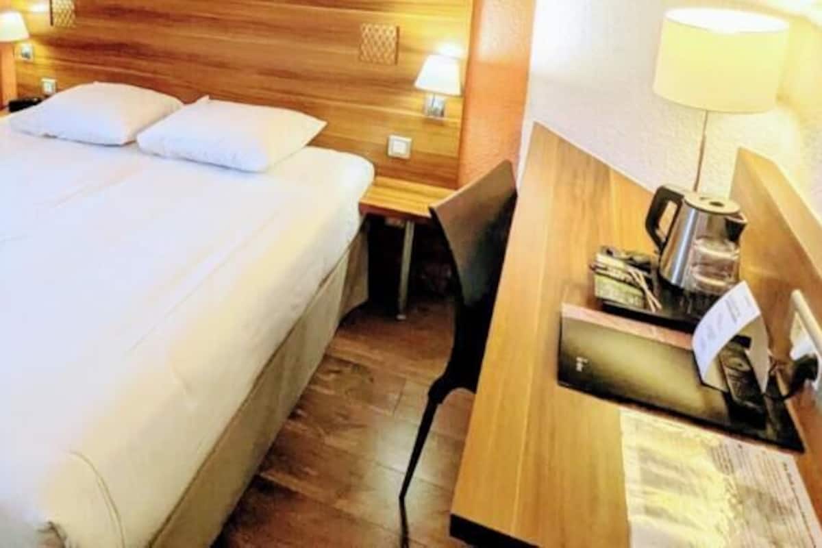 Una habitación de hotel con una cama grande, un escritorio con lámpara y un cabecero de madera.