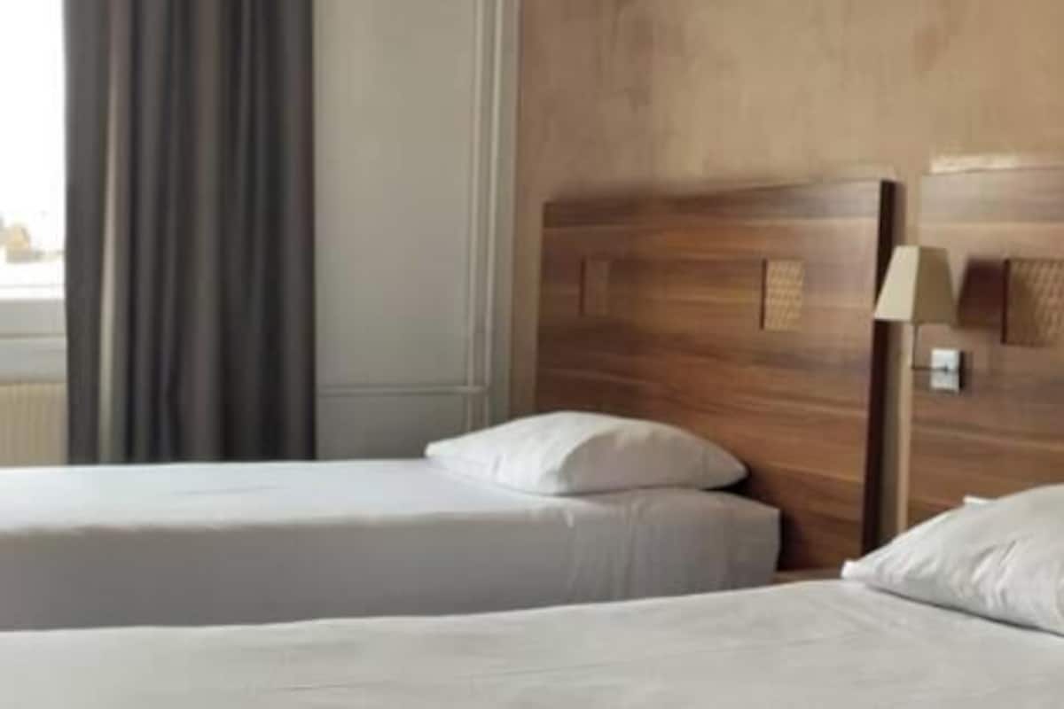 Habitación de hotel con dos camas individuales, un cabecero de madera, un escritorio y vistas a la ciudad.