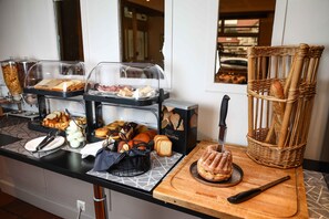 A breakfast buffet with various food items and a knife on a wooden cutting board. - The Originals City, Hôtel Colmar Gare (Colmar)