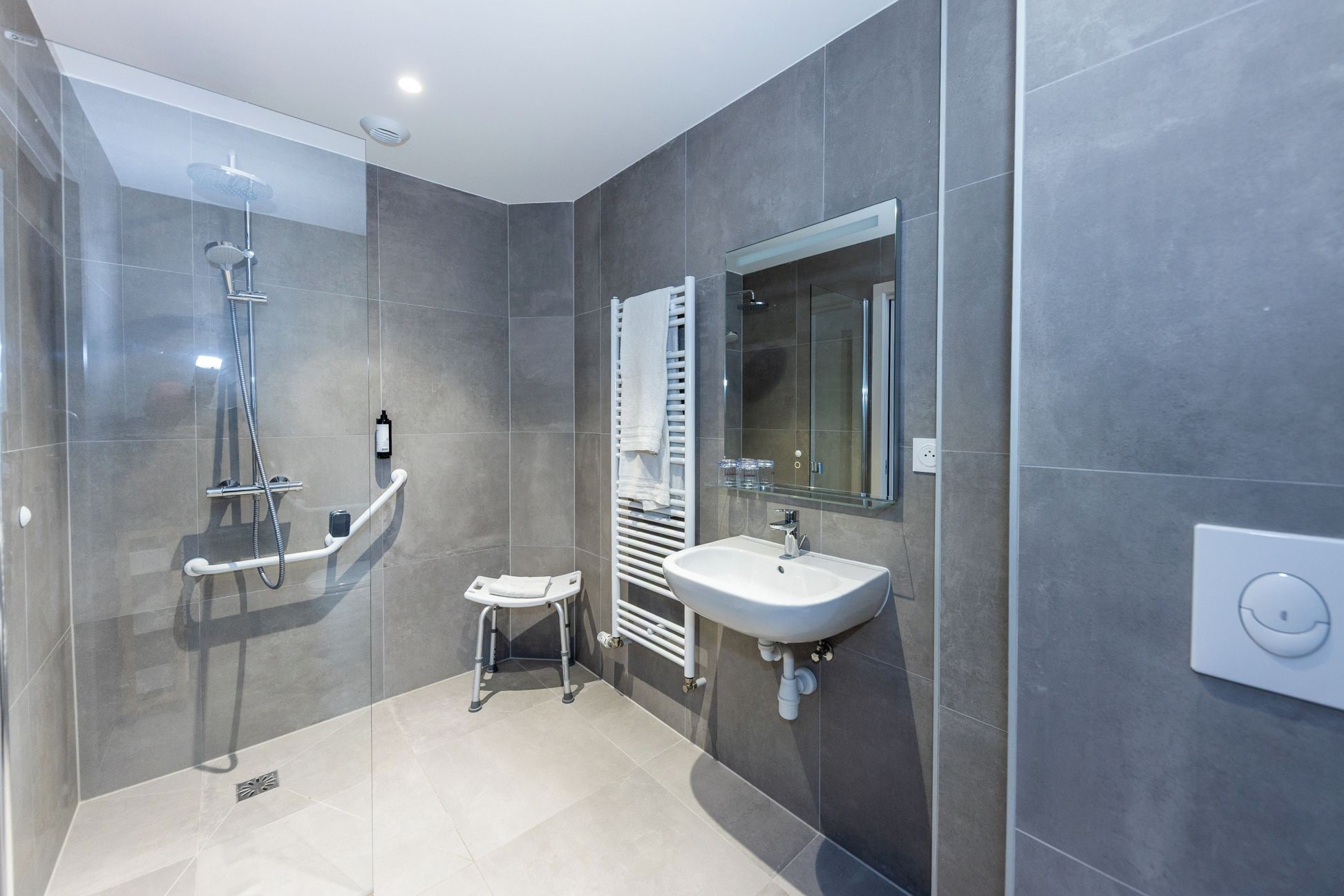 Un baño moderno con cabina de ducha de vidrio, un lavabo blanco y un perchero para toallas.