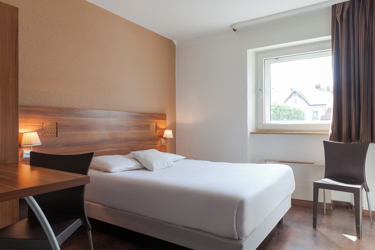 A hotel room with a bed, a desk, and a chair.
