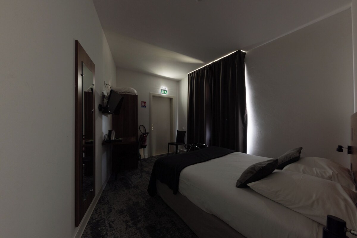 A hotel room with a bed, a desk, a chair, and a wardrobe.