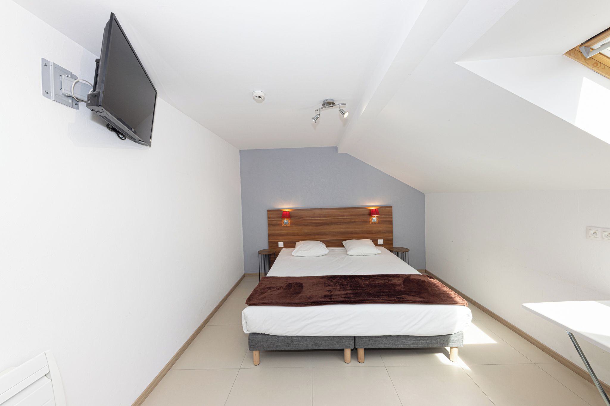 Un dormitorio moderno con cama, televisor montado en la pared y lámpara del techo.