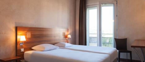 A hotel room with two beds, a nightstand with lamps, a chair, and a balcony with a view.