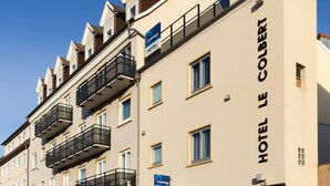 Un hôtel à plusieurs étages doté de balcons, une enseigne indiquant qu’il s’agit d’un hôtel, et un ciel bleu clair en arrière-plan.
