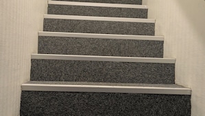 Un escalier dont les marches sont recouvertes de moquette et dont les rampes sont blanches, menant à l’étage supérieur.