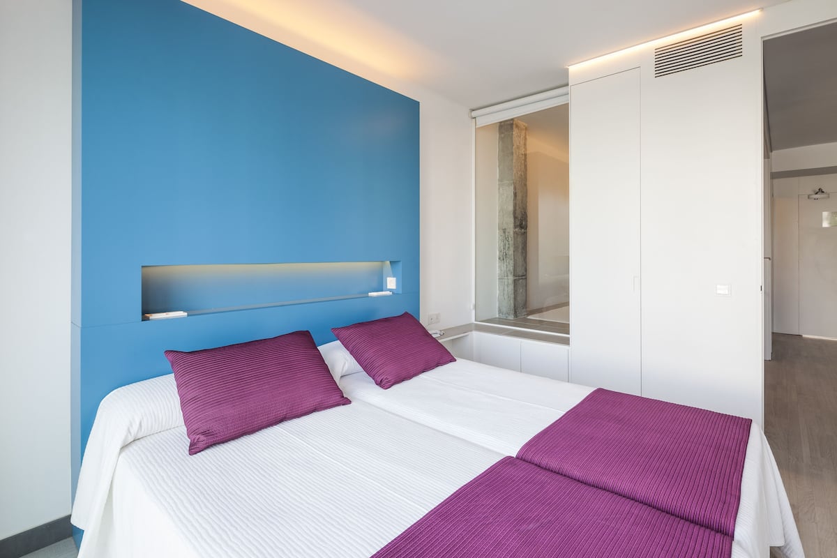 A modern hotel room with a large bed, a blue accent wall, and a window with a view.