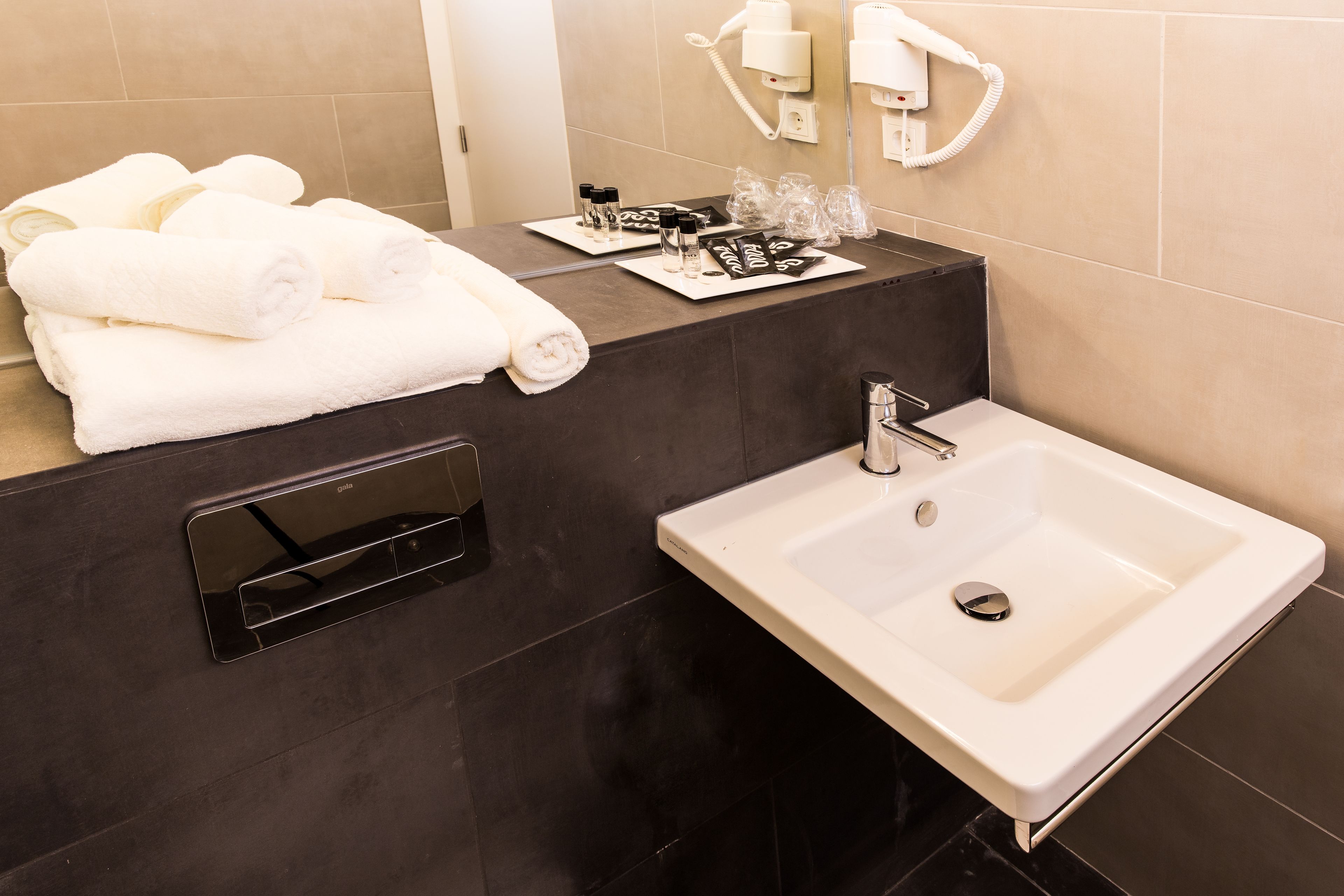 Un baño moderno con un lavamanos grande, un perchero con toallas dobladas y artículos de aseo en la encimera.