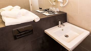 A modern bathroom with a large sink, a towel rack with folded towels, and toiletries on the counter.