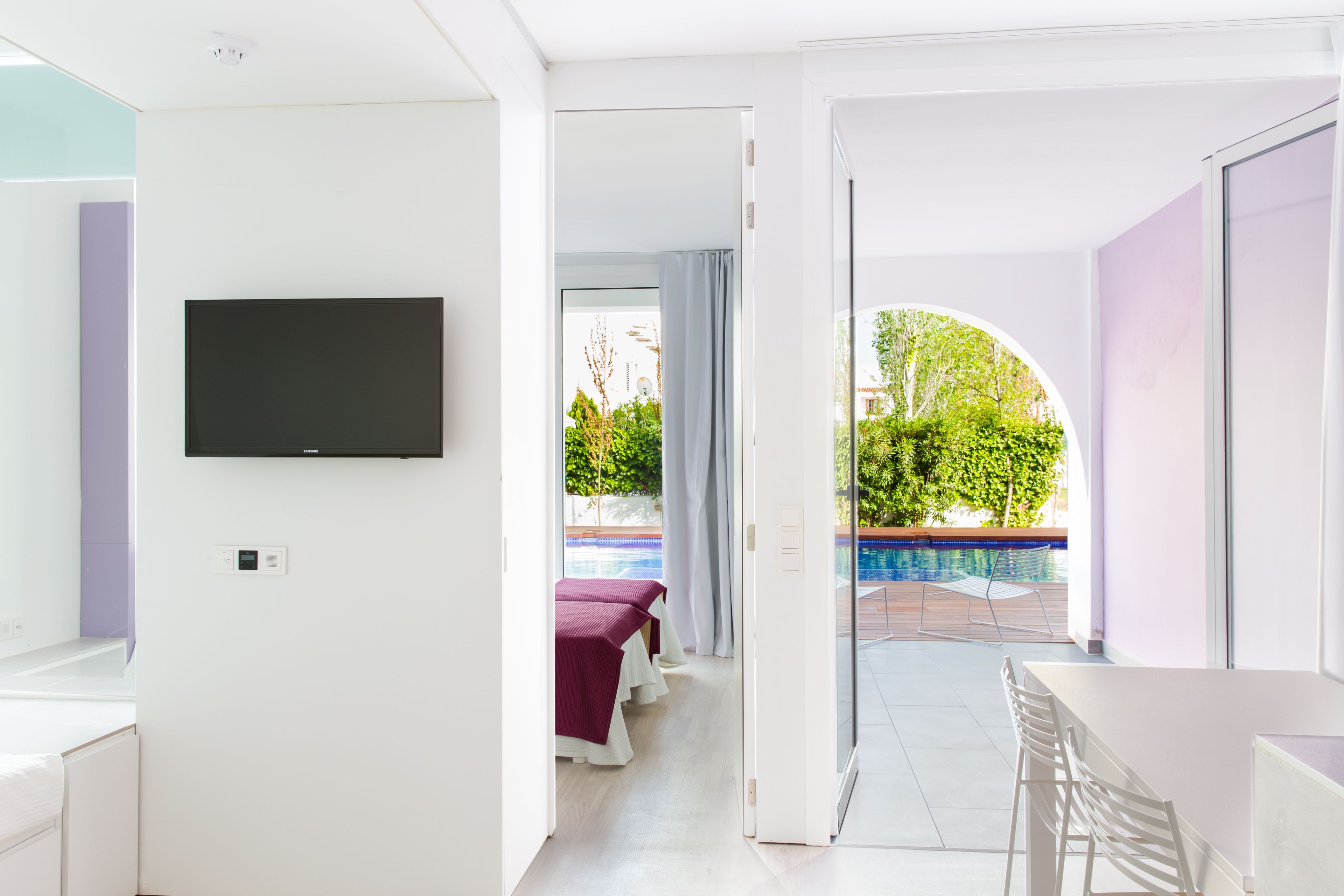 Une chambre d’hôtel moderne dotée d’un téléviseur à écran plat fixé au mur, d’un balcon avec vue sur la piscine et d’un coin repas avec une table et des chaises.