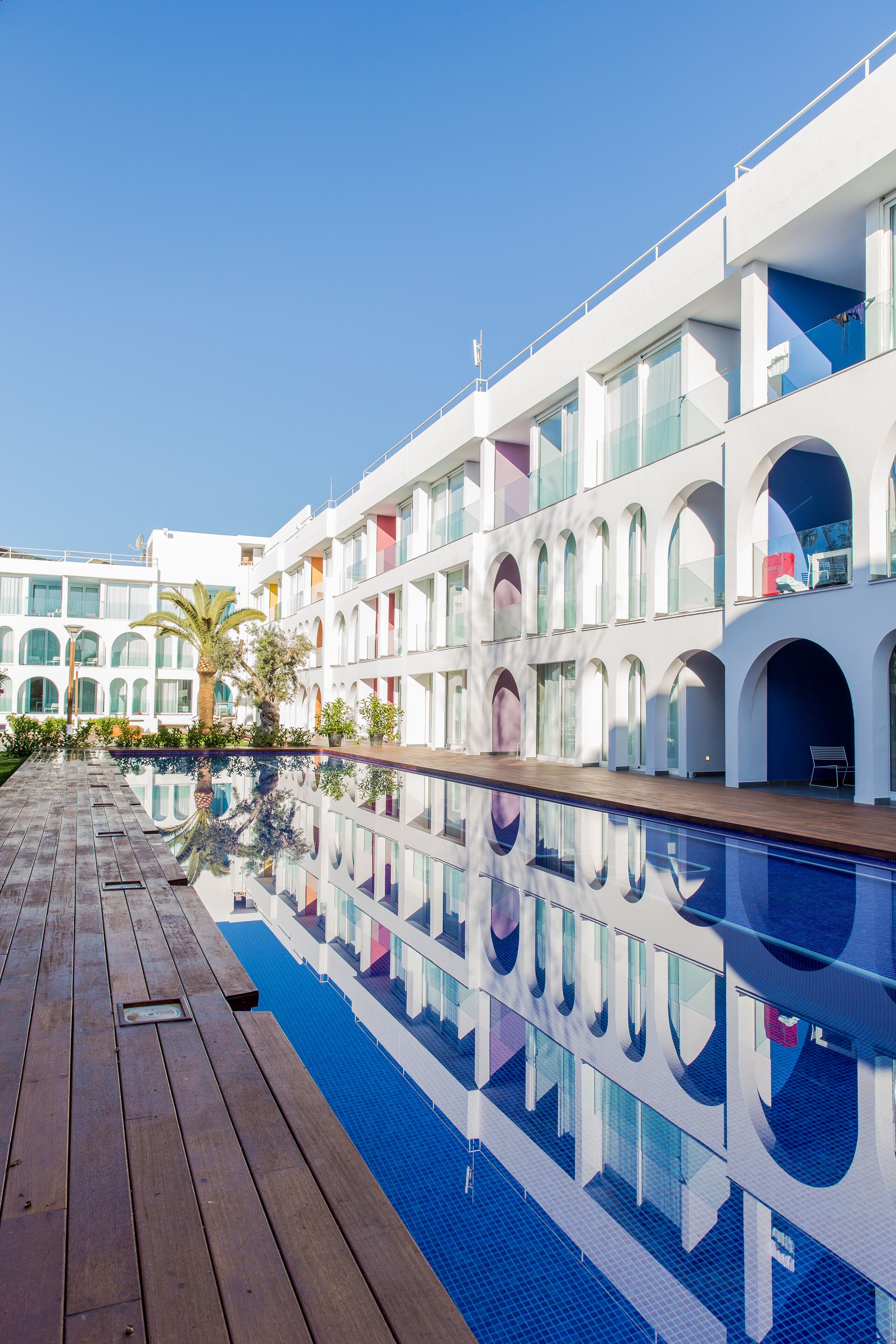A modern hotel with a pool, wooden deck, and multiple balconies.