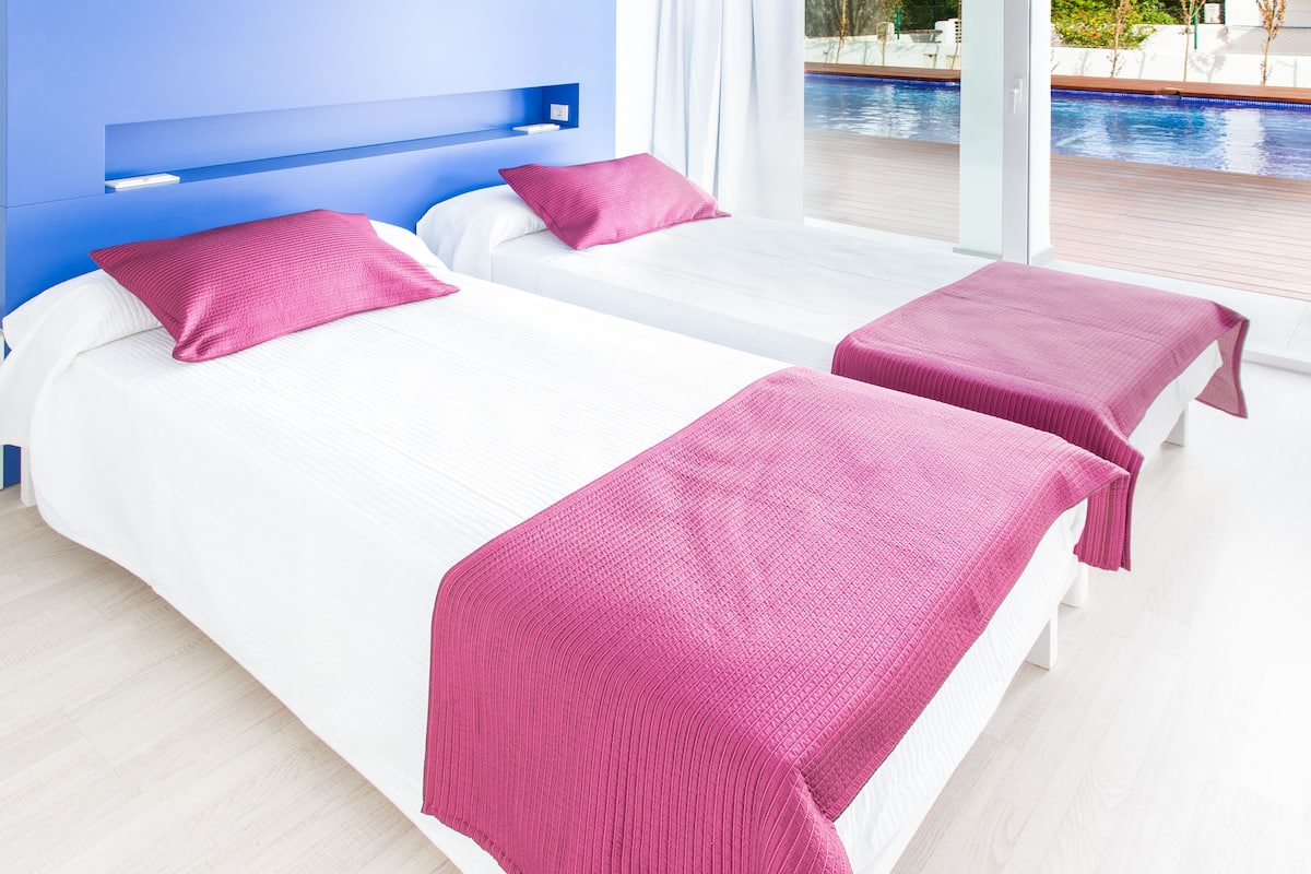 A hotel room with two beds, each with a white mattress and a pink blanket.