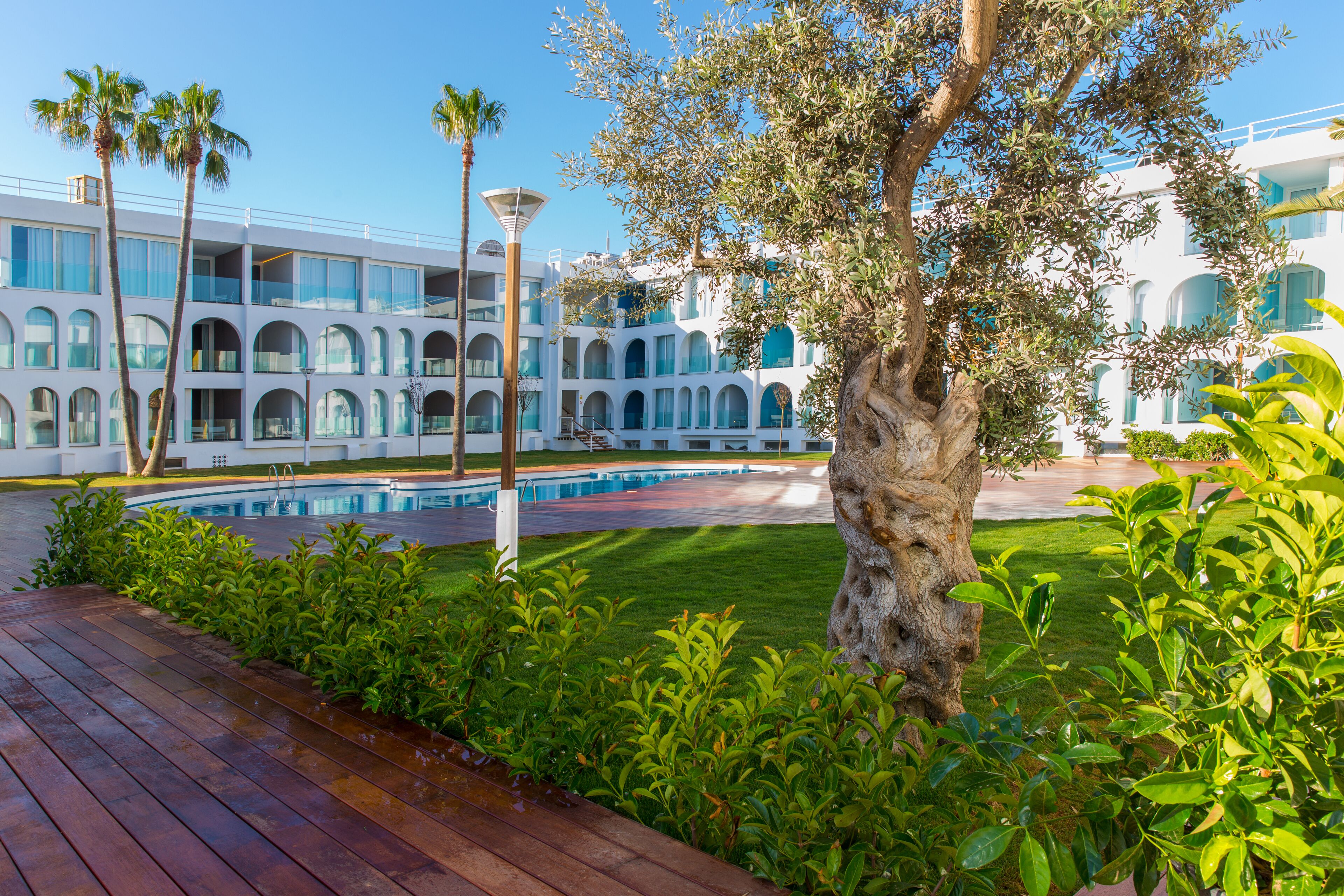 A modern hotel with a pool, outdoor seating, and lush greenery.