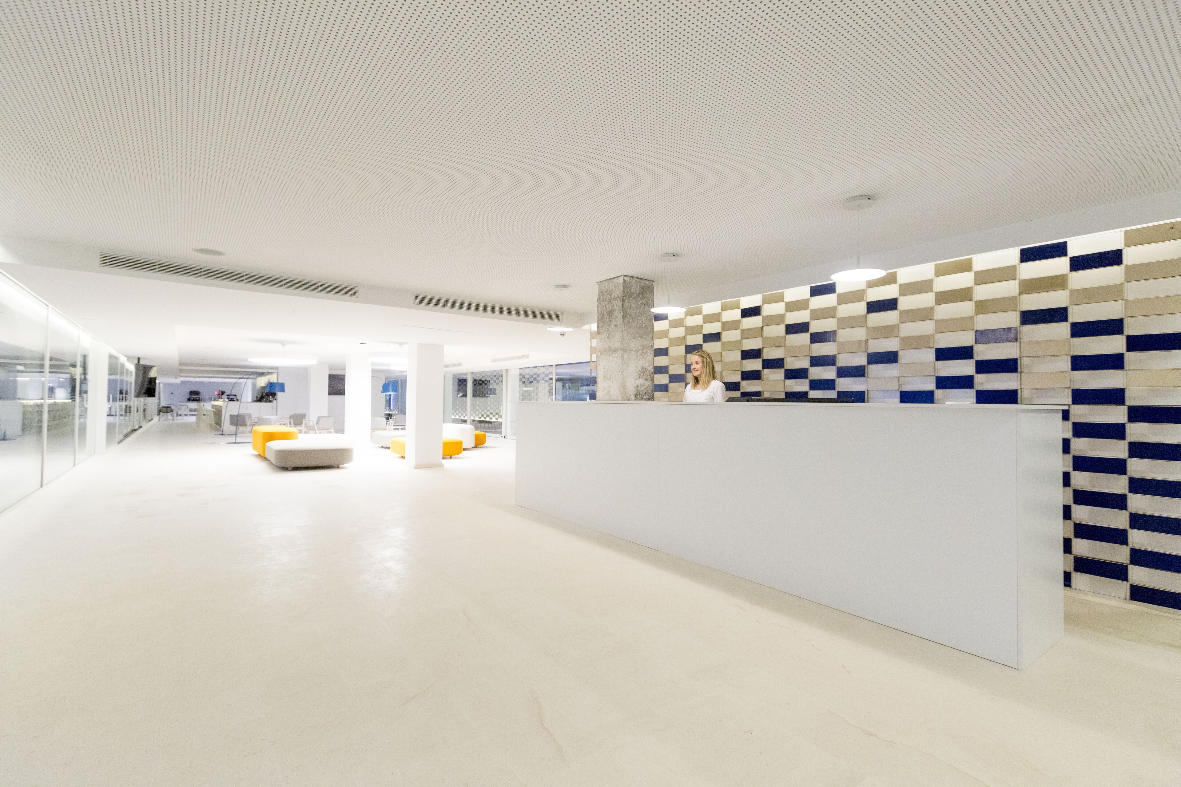 A modern reception area with a checkered wall, a white reception desk, and a glass partition.