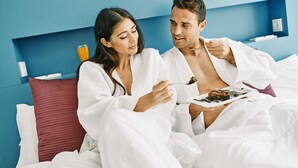 A couple in a hotel room, both wearing white robes, eating breakfast. - Ebano Hotel Apartments & Spa (Sant Josep de sa Talaia)