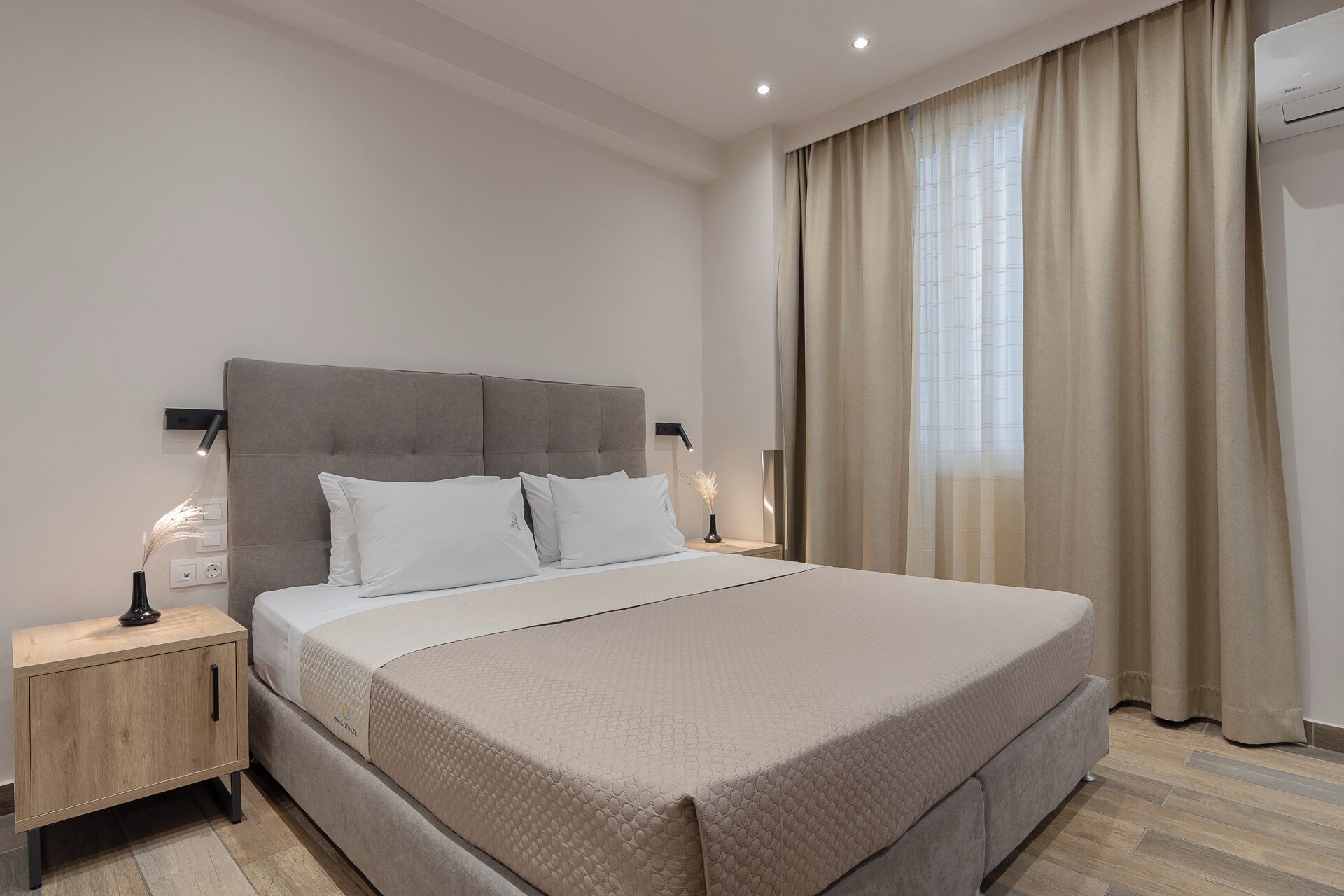 A modern bedroom with a large bed, two bedside tables, a headboard, and a window with curtains.