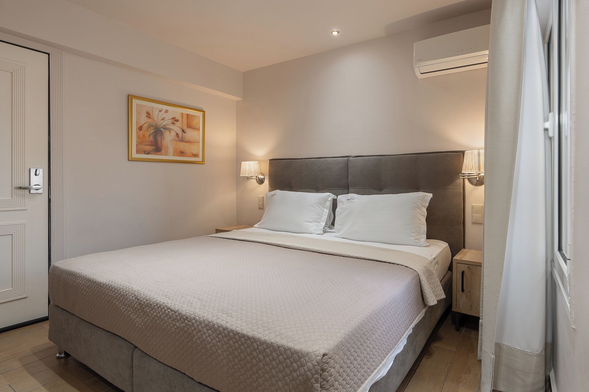 Een hotelkamer met een bed, nachtlampjes, een airconditioning en een schilderij aan de muur.