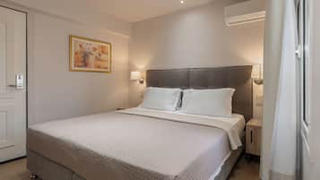 Una habitación de hotel con una cama, lámparas de noche, un equipo de aire acondicionado y un cuadro en la pared.