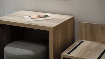 A small wooden table with a magazine on it, a grey upholstered stool, and a wooden chair with a black stripe.